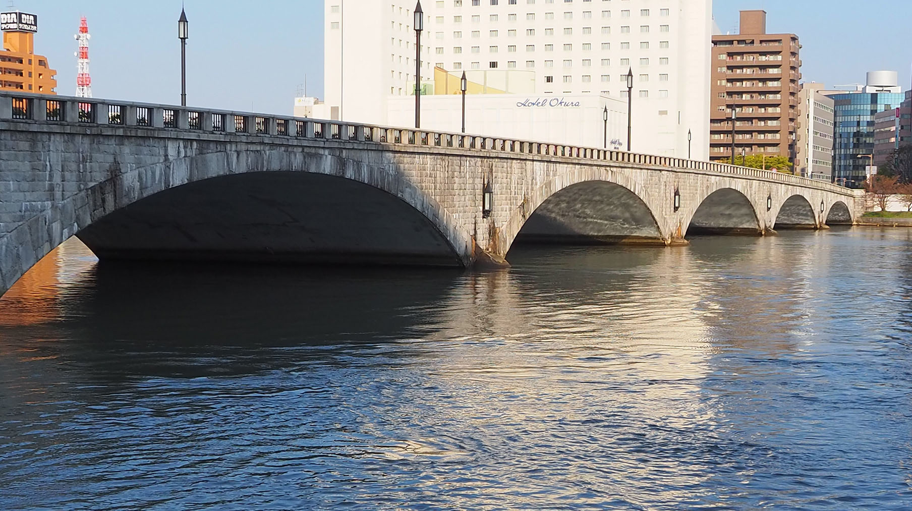 拠点としている新潟市を映した写真。夕暮れ前の日差しにきらめく信濃川と万代橋が映っている。